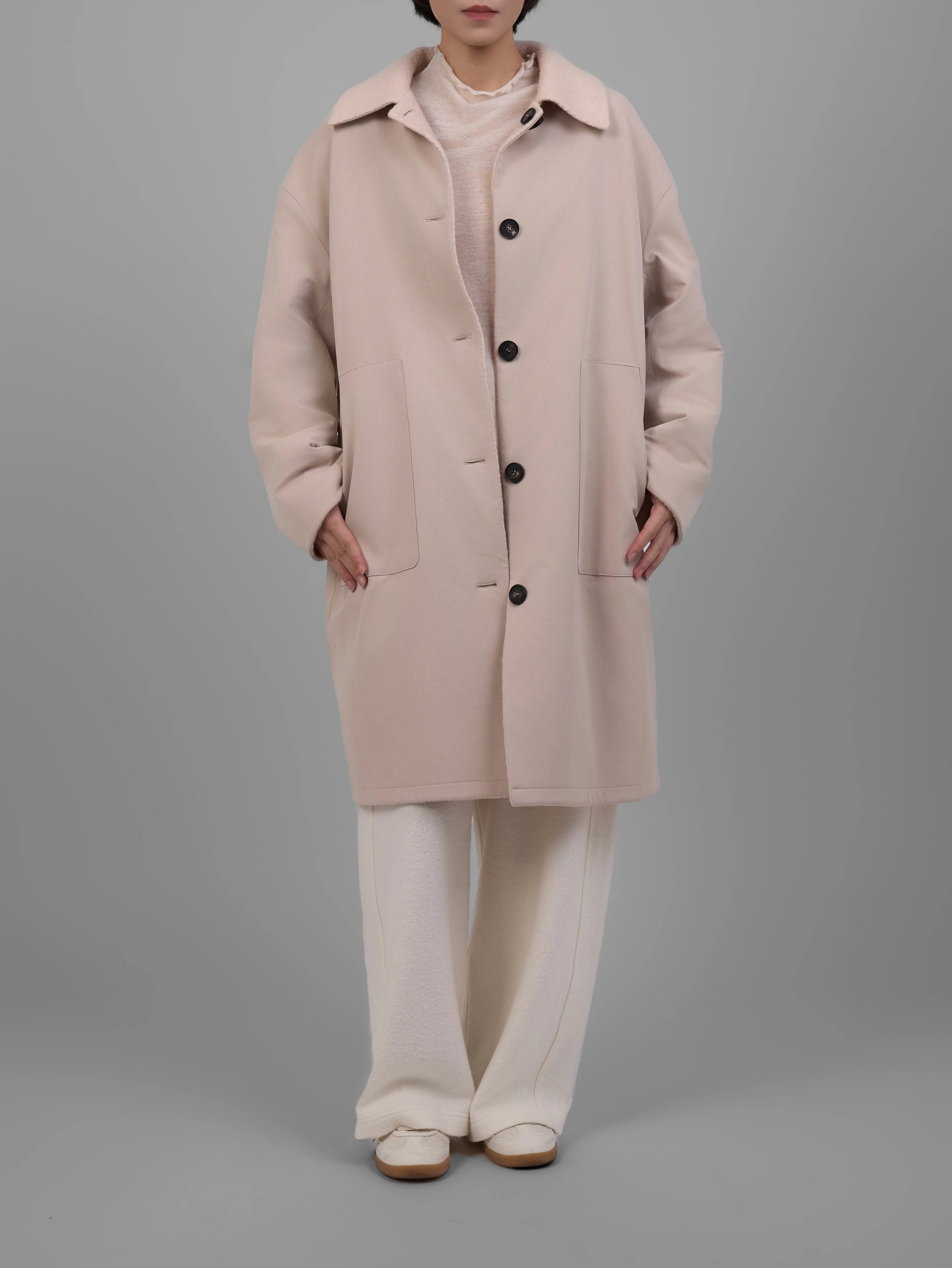 Model wearing reversible cream wool coat, straight front stance with button closure.