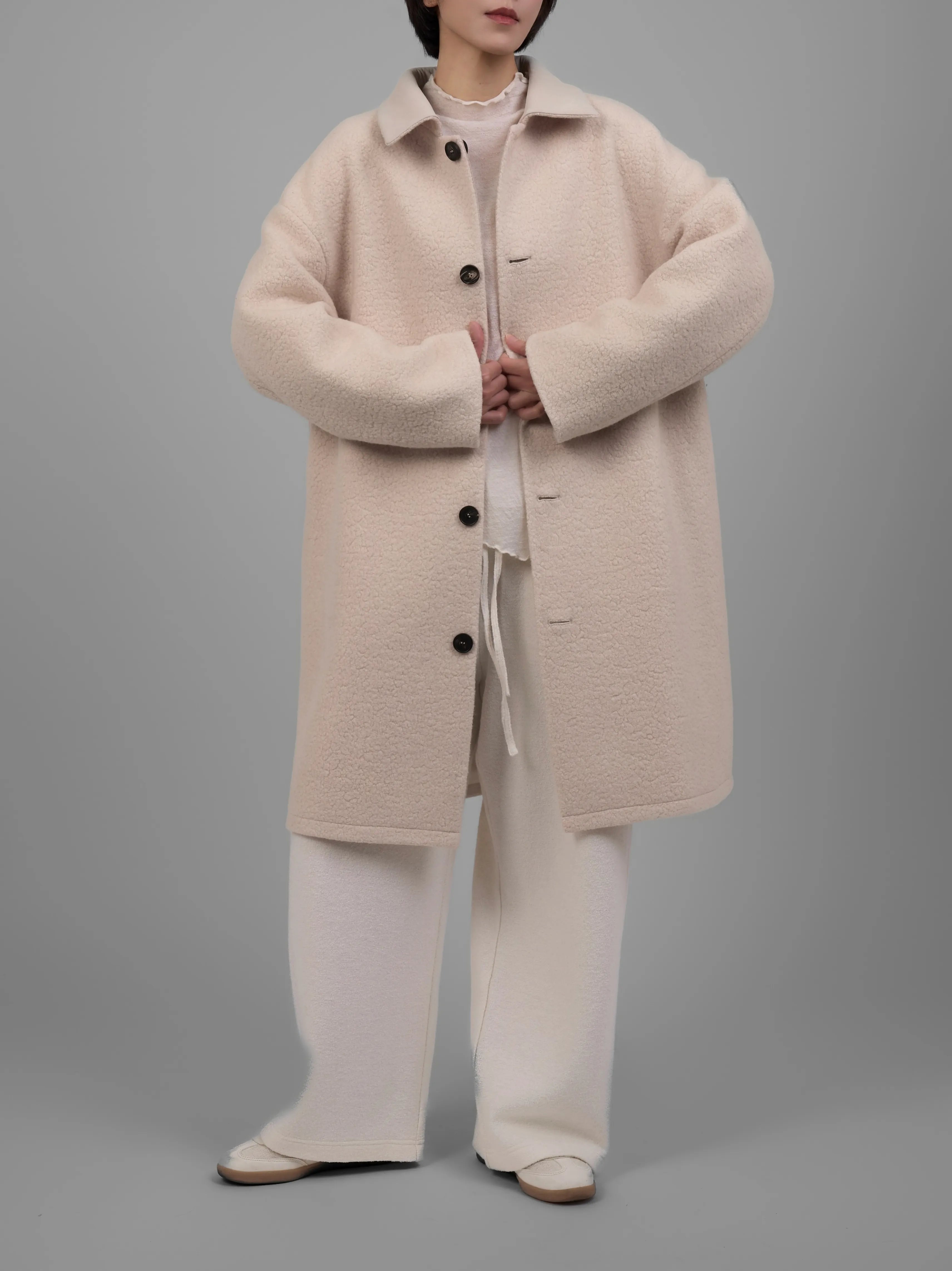 Cream reversible wool coat shown in mid-length front view with pockets and rounded sleeves.