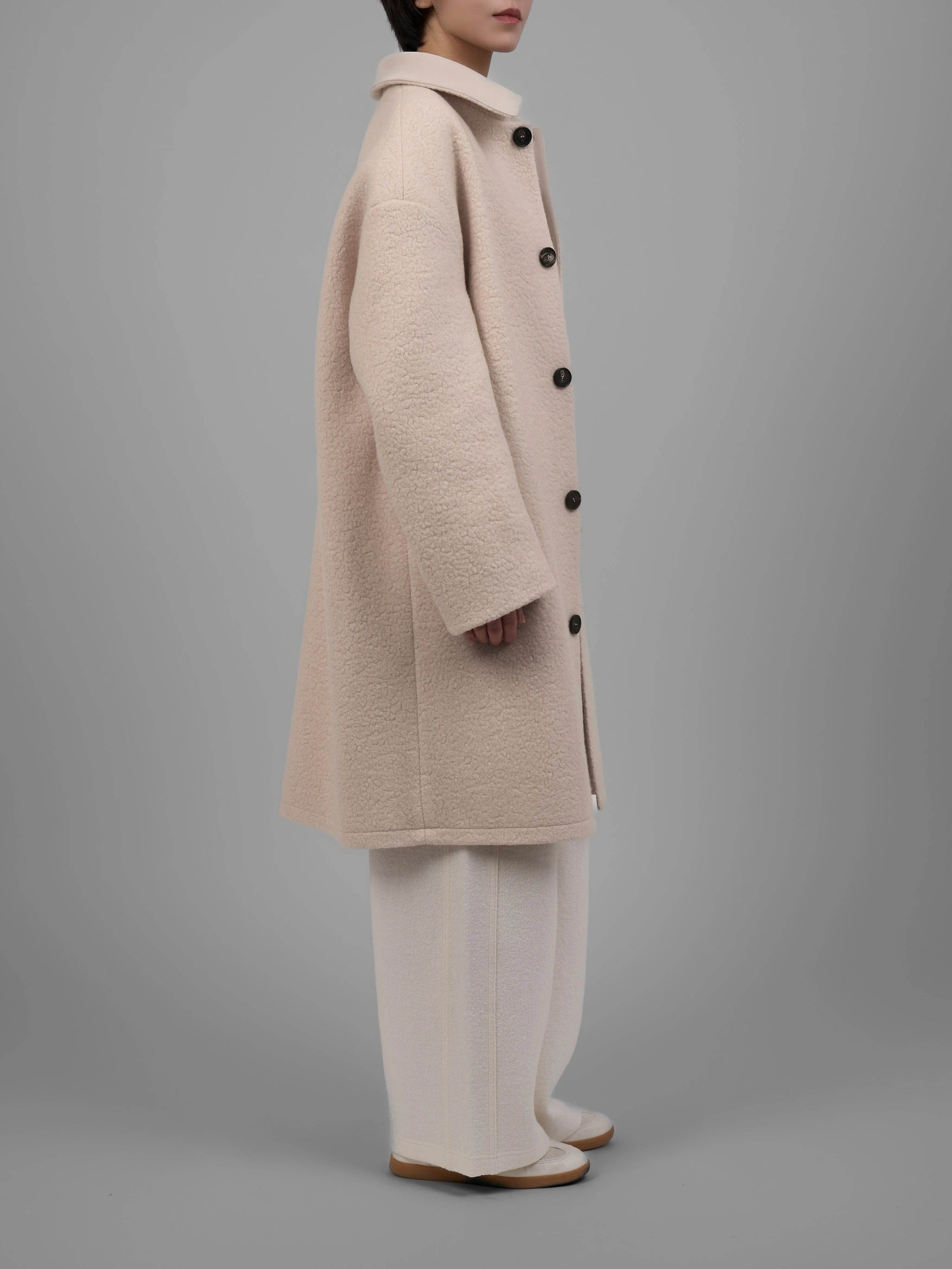 Side view of reversible cream wool coat showcasing dropped shoulders and clean tailoring.