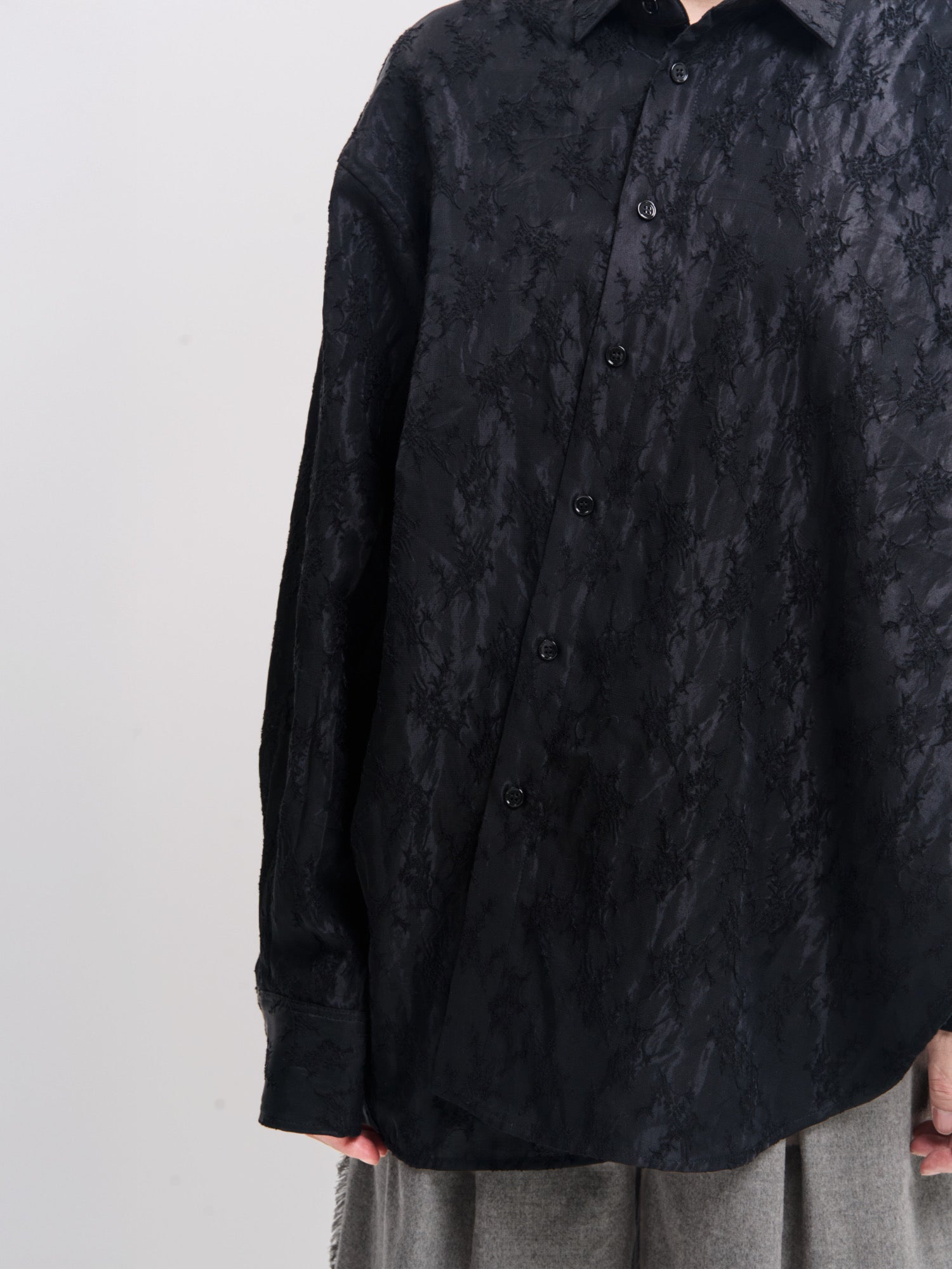 Close-up front view of black textured shirt showing fabric texture and relaxed silhouette.