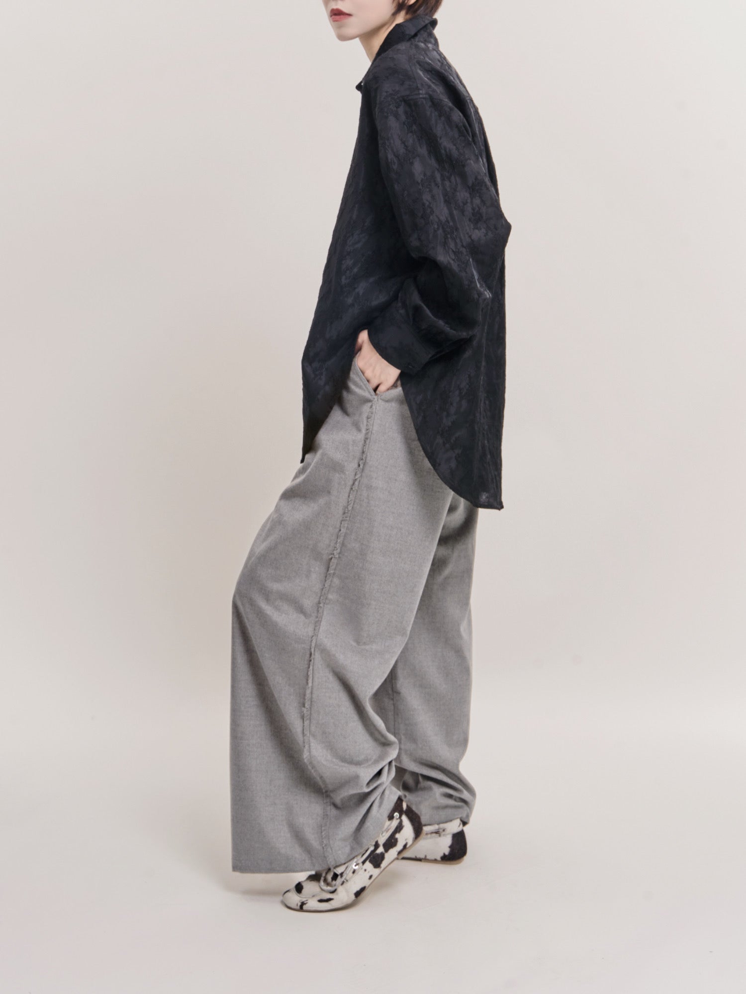 Side view of black textured shirt styled with grey wide-leg trousers, relaxed cocoon fit in studio light.