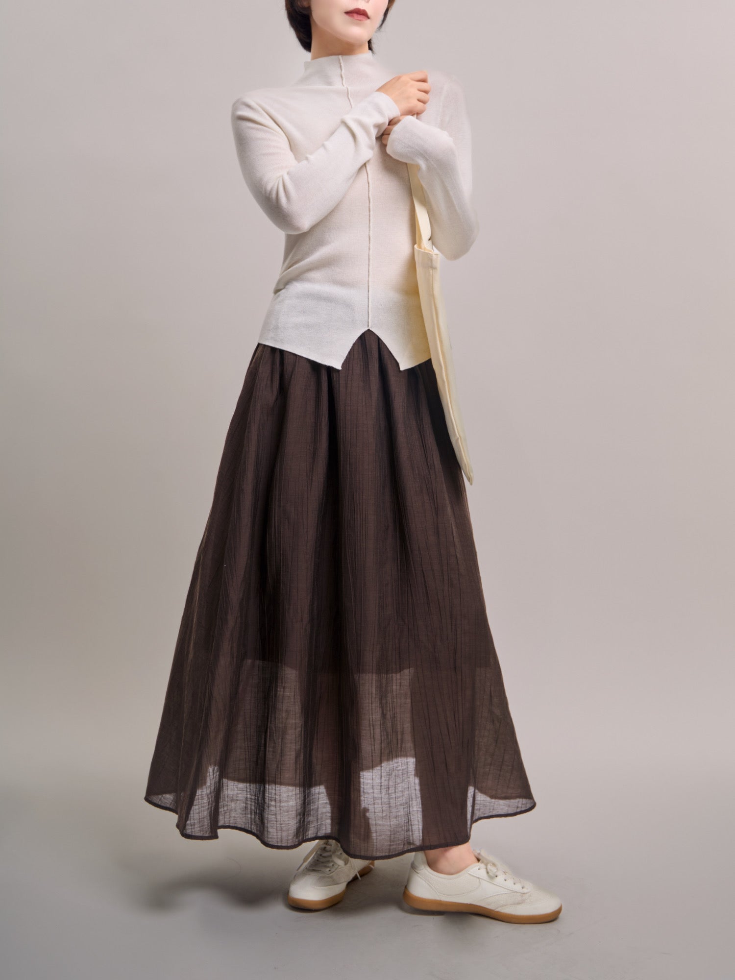 Model wearing dark brown Veil Pleats Skirt, full-body studio shot showing sheer layered hem and fluid pleats.
