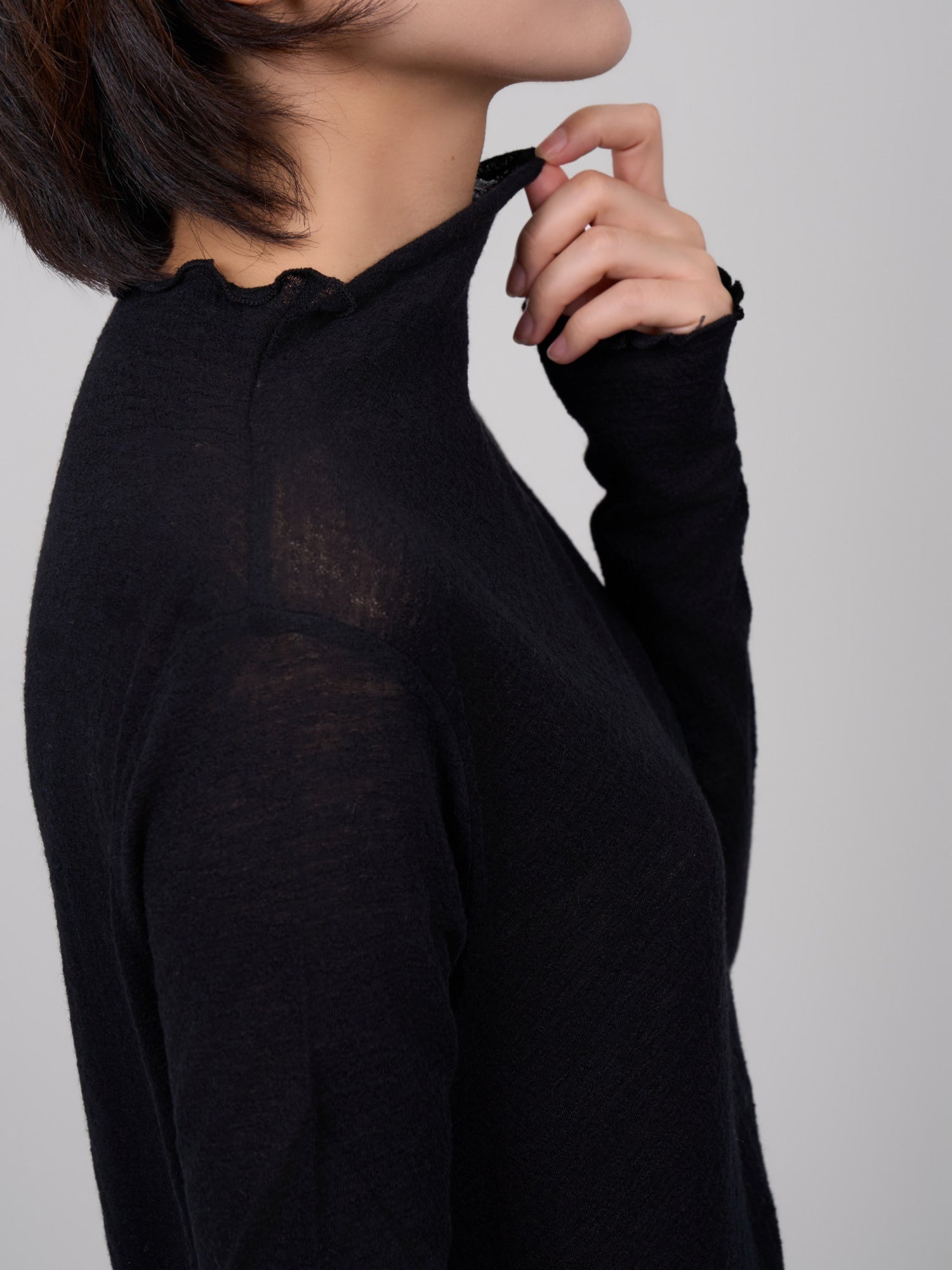 Side close-up of black wool base layer showing raw-edge collar and fine wool texture.