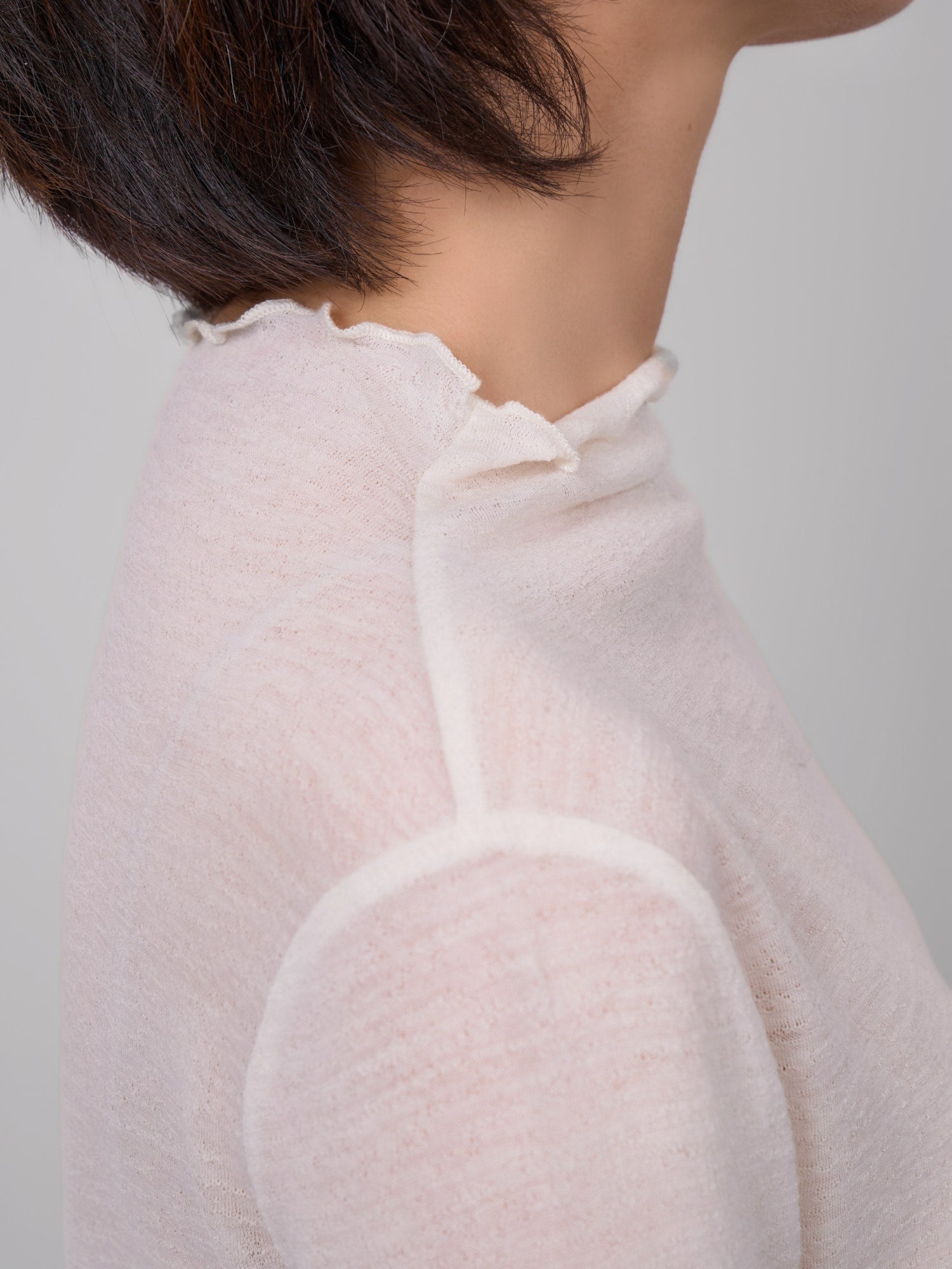 Close-up side neckline detail of white wool base layer, showing clean raw edge and soft breathable knit.