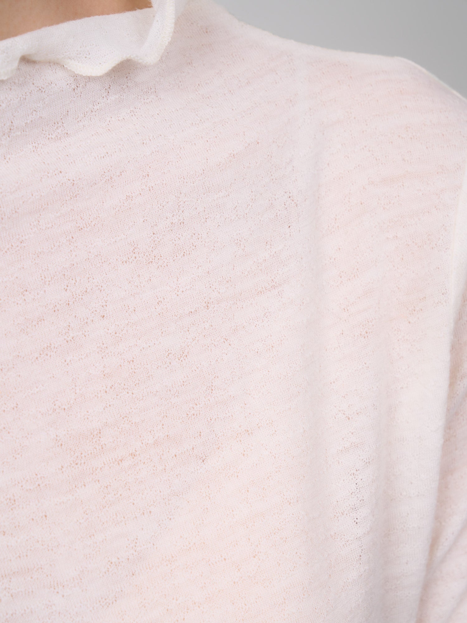 Shoulder seam detail of white wool base layer, highlighting fine stitching and soft sheer wool finish.