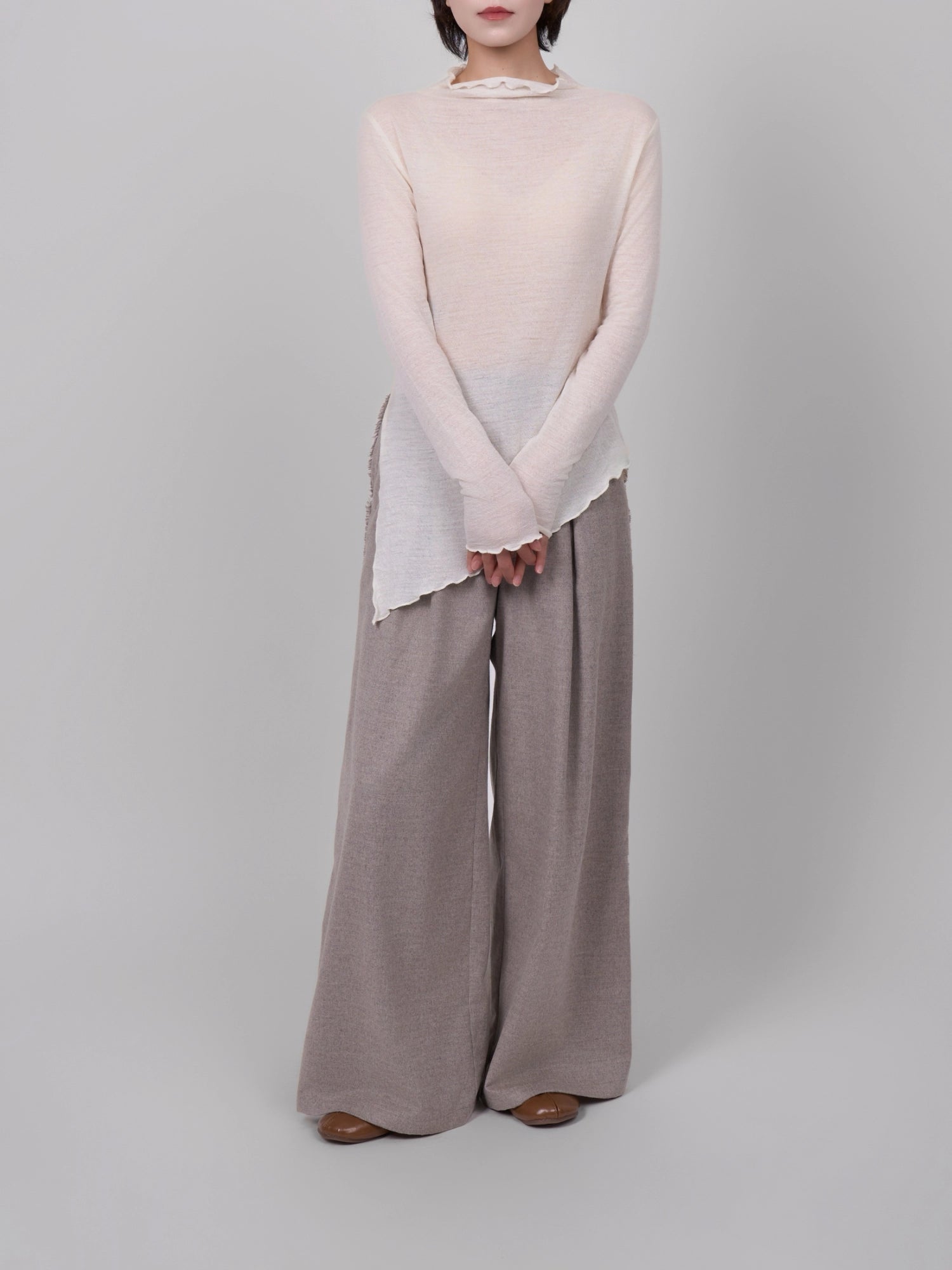 Model wearing white 100% wool base layer with asymmetric hem, full-body studio shot styled with wide-leg trousers.