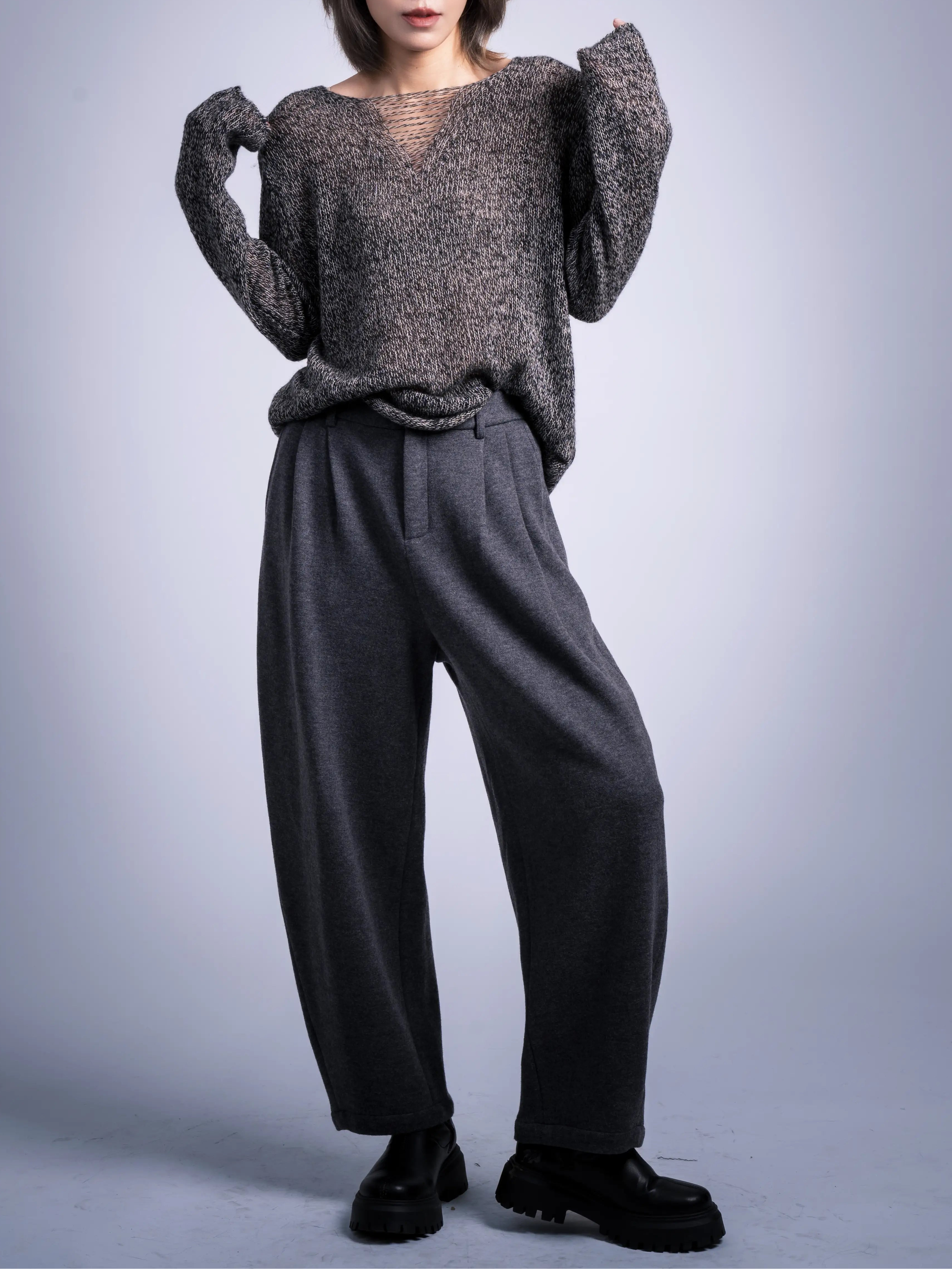 Model wearing brown wool jumper with relaxed French drape, styled with charcoal cocoon trousers in a studio full-body pose.