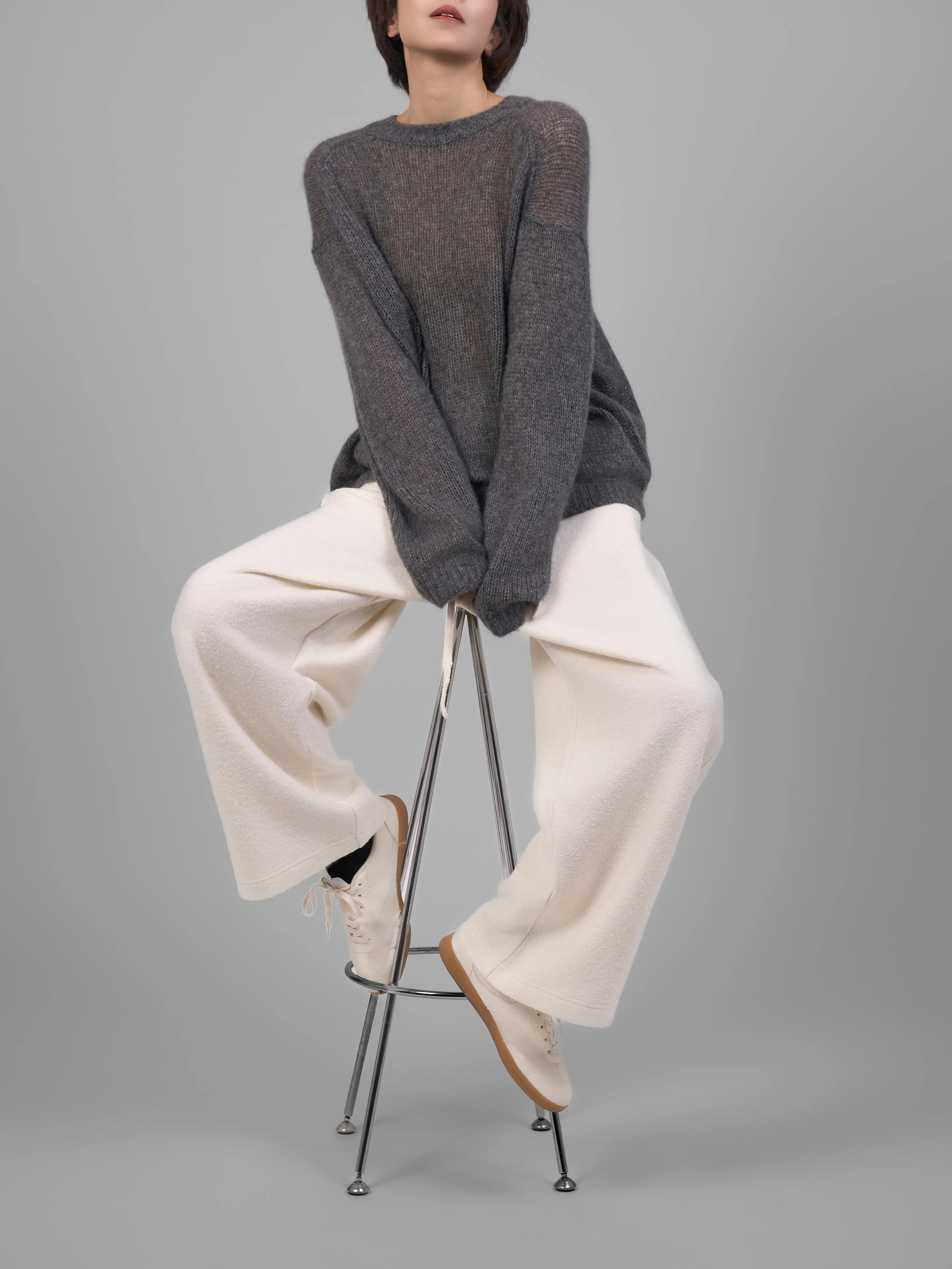 Grey wool-blend knit trousers in seated studio pose showing drape and fit.