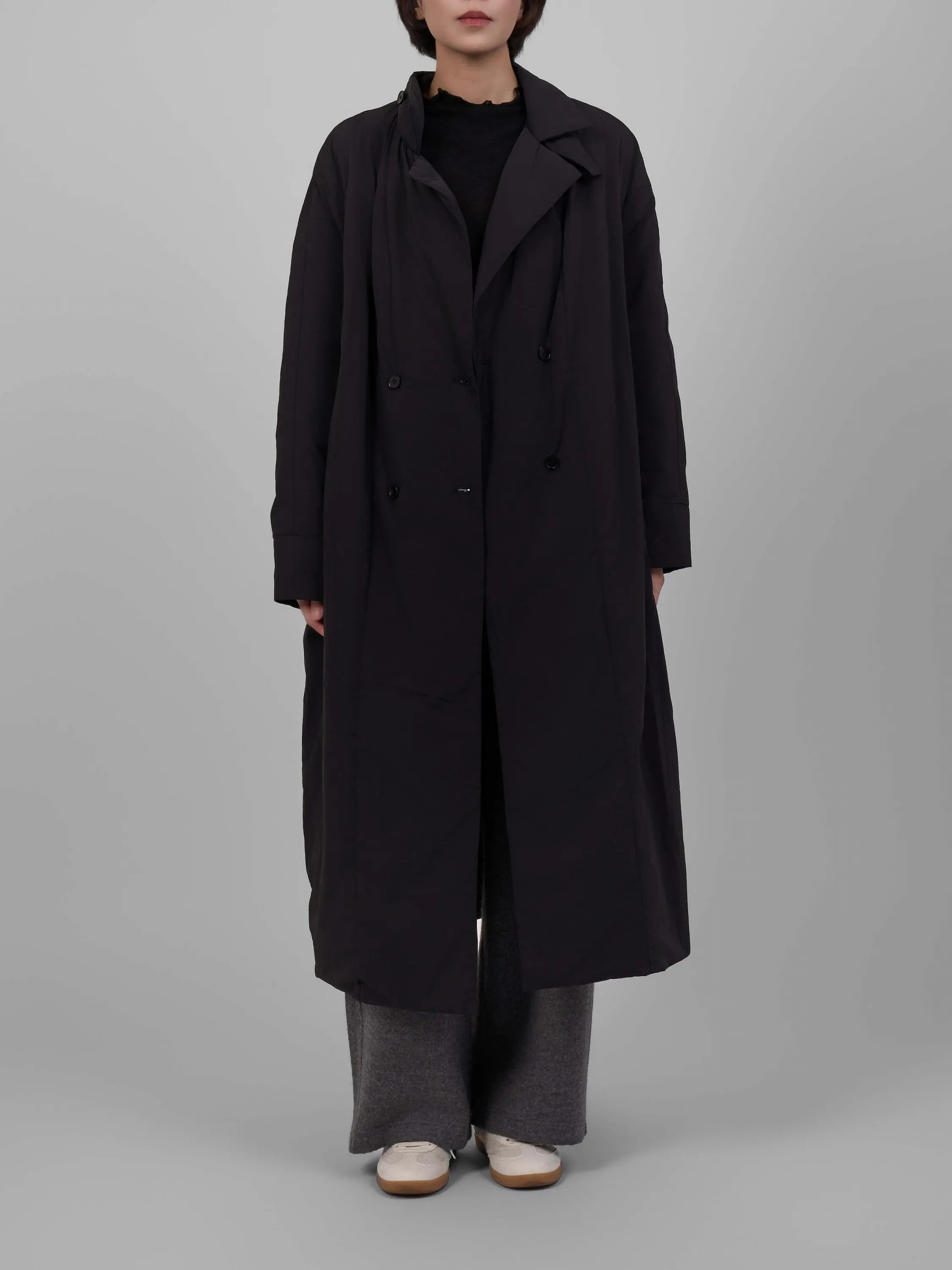 Person wearing a long black coat on a gray background