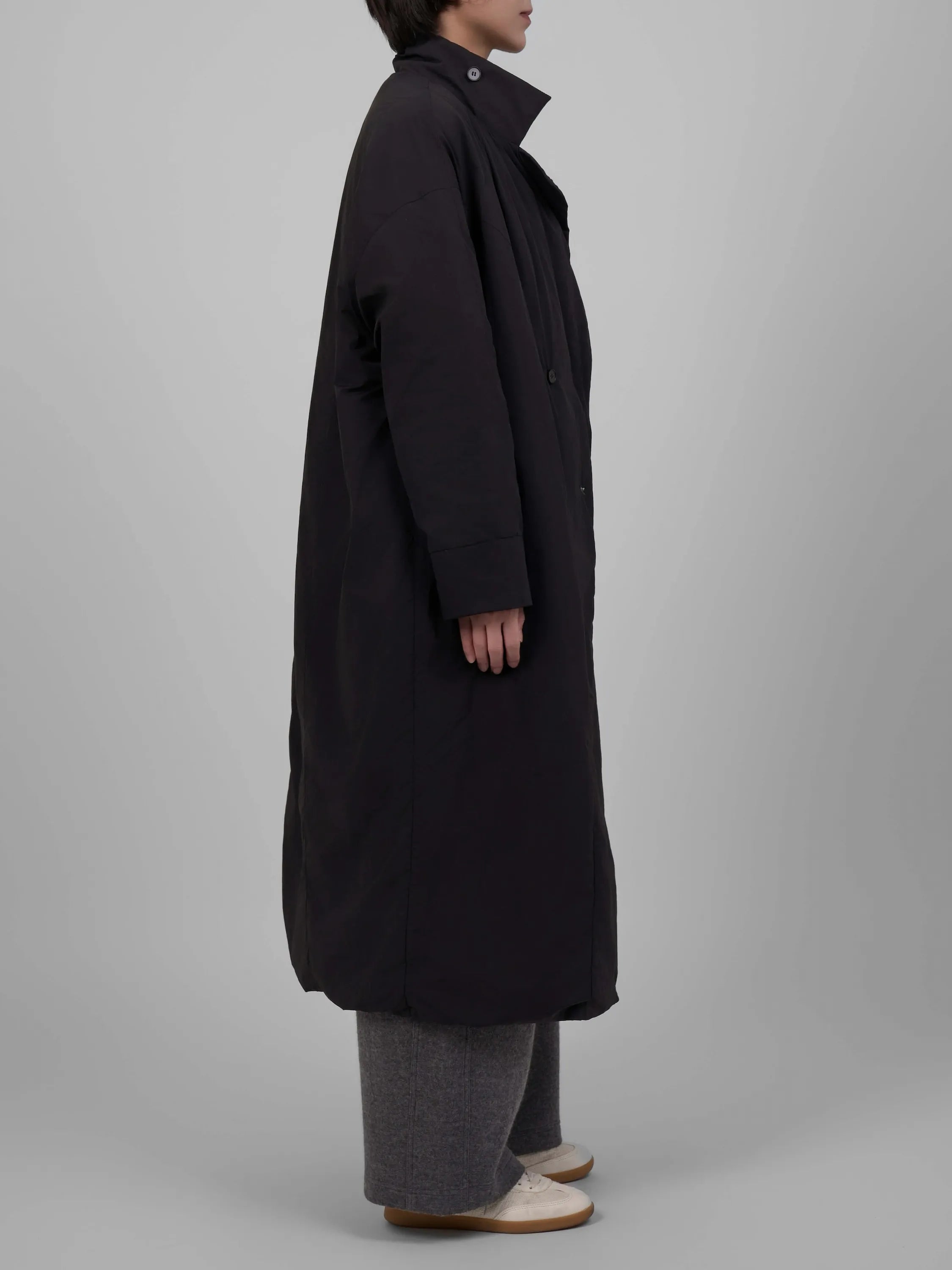 Person wearing a long black coat on a plain background