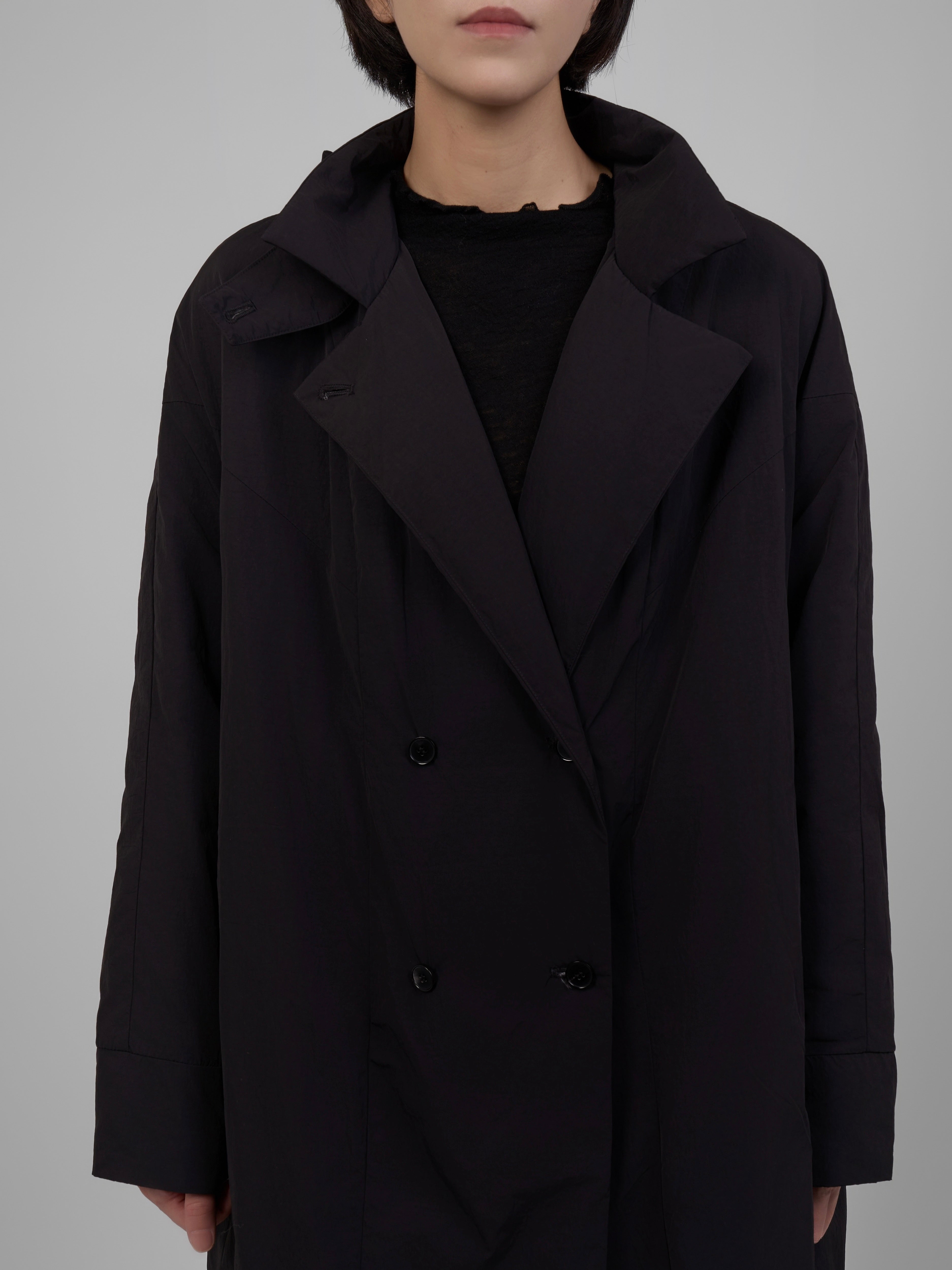 Person wearing a black coat against a gray background
